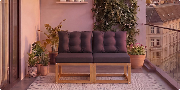 Двуместен модулен дървен диван с тъмносиви възглавници на балкон, заобиколен от саксийни растения и изглед към града на заден план